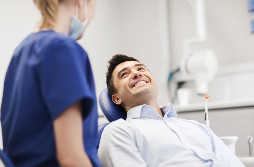 Smiling patient sitting in dental chair next to dental hygienist